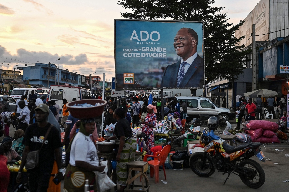 Customers and vendors stand next to a campaign billboard for Ivorian President and presidential candidate for Rally of Houphouetists for Democracy and Peace Alassane Ouattara at a market in Abobo, a suburb of Abidjan. (AFP)