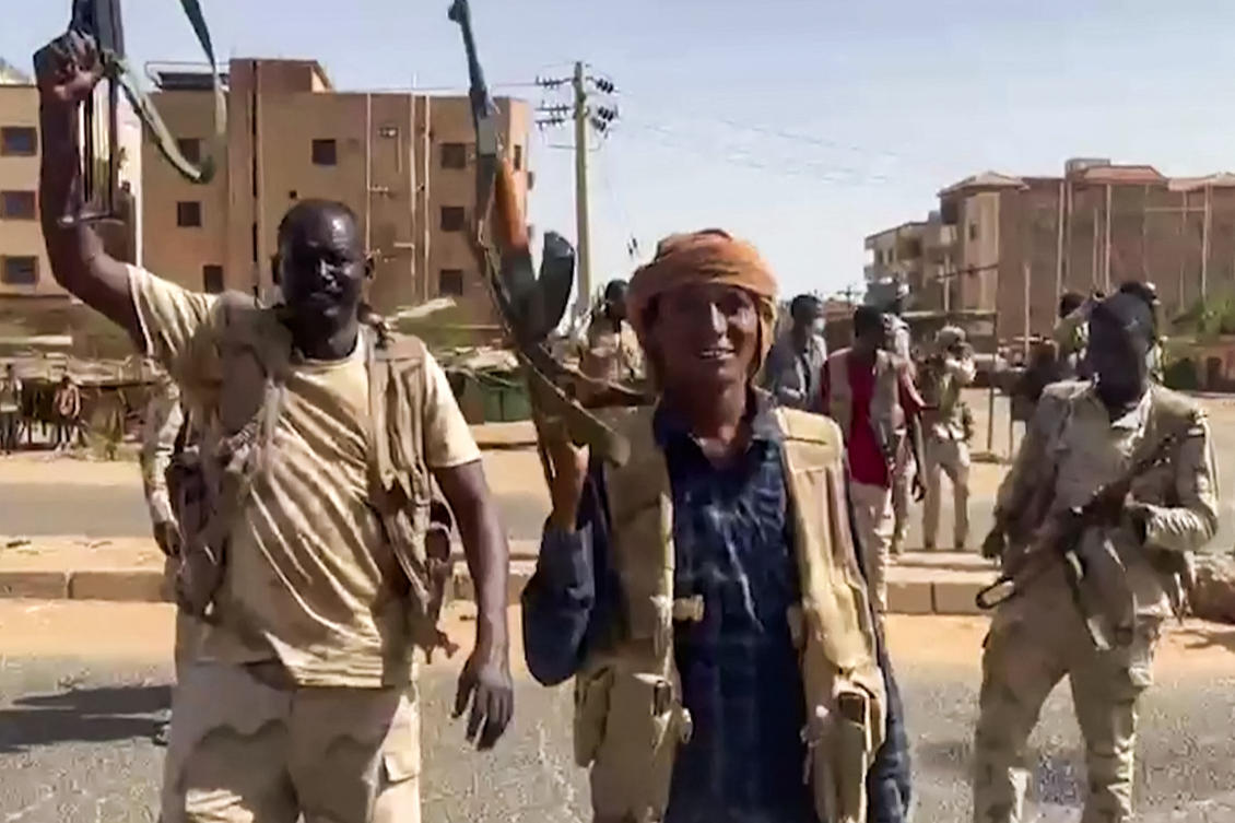 The Sudanese paramilitary Rapid Support Forces (RSF) on April 23, 2023, fighters wave assault rifles as they cross a street in the East Nile district of greater Khartoum. (AFP)