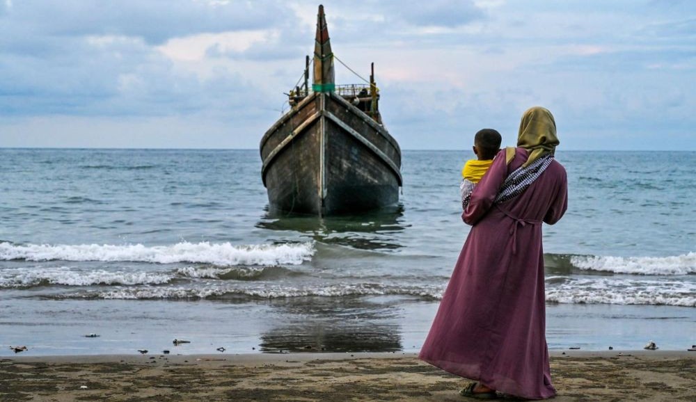 A woman with her child looks at a boat which carried Rohingya refugees to a beach in Aceh, Indonesia, Dec. 10, 2023. (AFP)