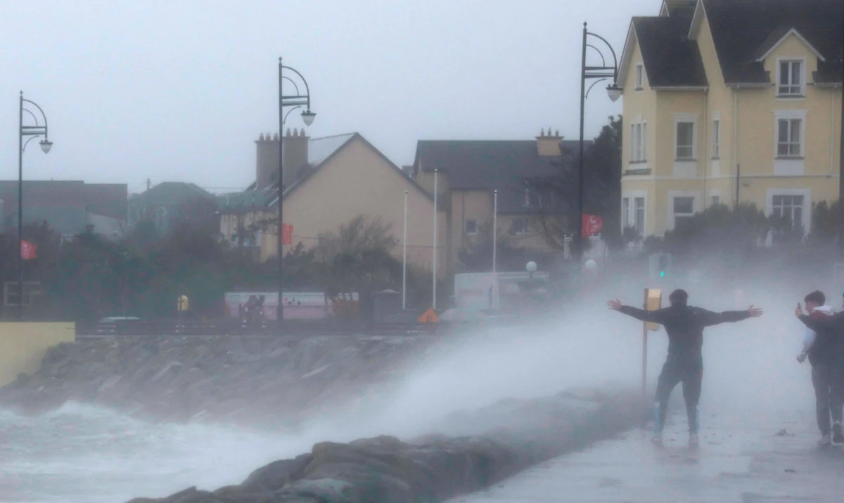 People stand in front of waves during Storm Amy which brought severe weather, in Galway, Ireland, October 3, 2025. (Reuters)