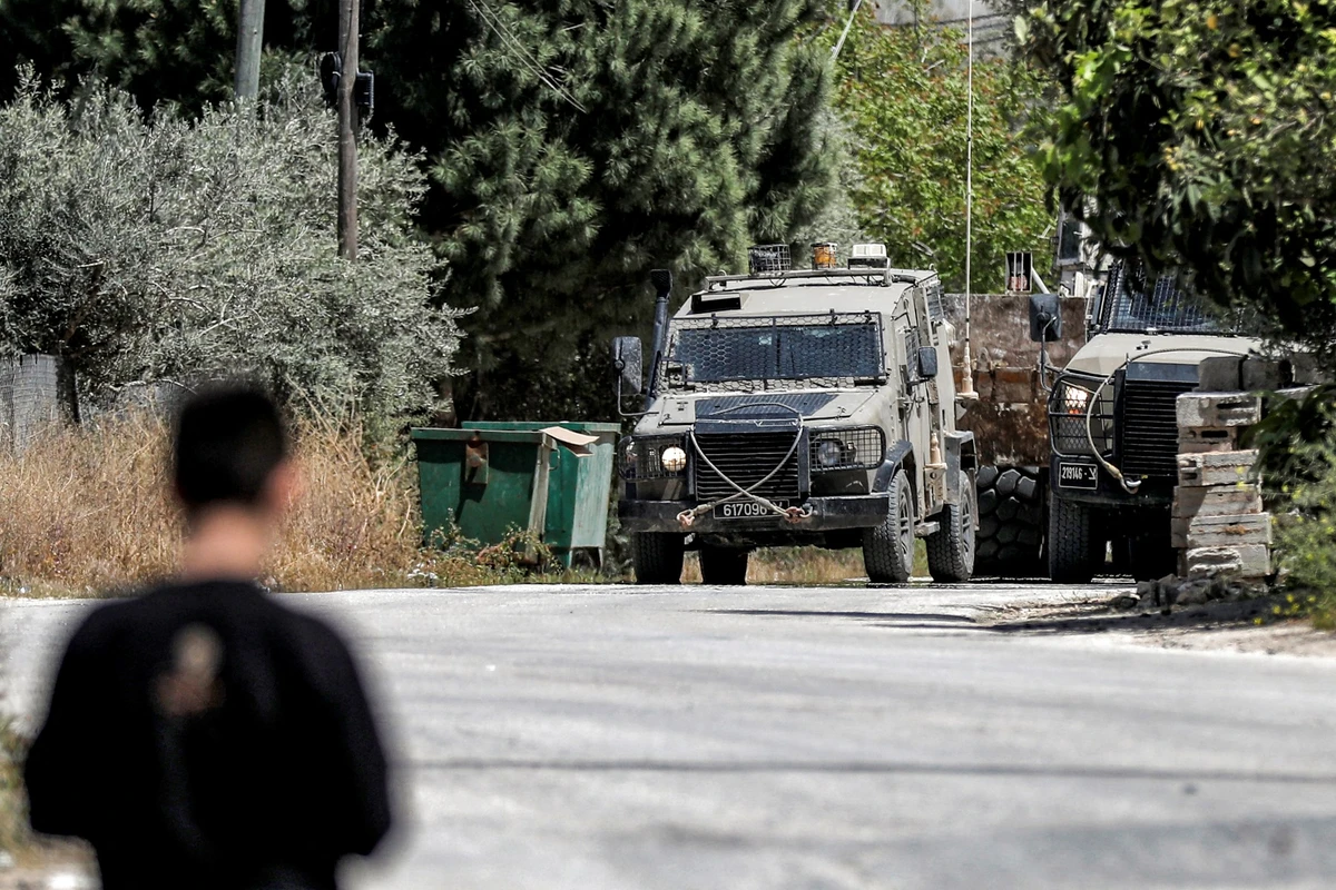 A man looks on as Israeli military armored vehicles are pictured during an army operation in the village of al-Misliyah, south of Jenin in the northern occupied West Bank, Apr. 16, 2025. (AFP)
