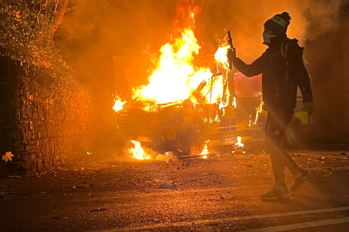 A protester films and a police vehicle burns in the background as a demonstration outside a hotel housing asylum seekers turns violent in Saggart, south-west of Dublin in Ireland on Oct. 21, 2025. (AFP)
