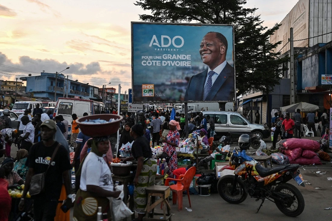 Customers and vendors stand next to a campaign billboard for Ivorian President and presidential candidate for Rally of Houphouetists for Democracy and Peace Alassane Ouattara at a market in Abobo, a suburb of Abidjan. (AFP)