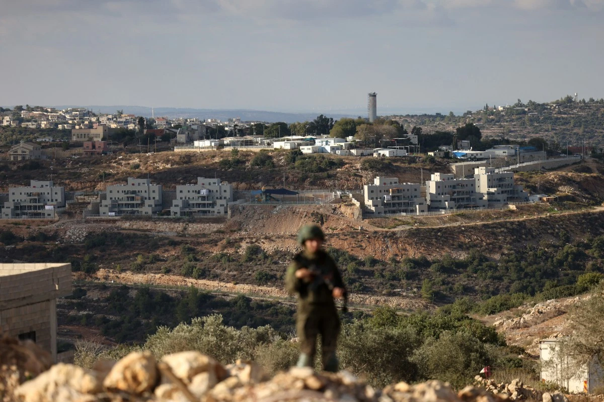 A member of the Israeli security forces stands guard, overlooking the Nahliel settlement (in the background), as security forces block Palestinians from reaching their land to harvest olives, in the village of Kobar, near Ramallah, in the Israeli-occupied West Bank, Oct. 18, 2025. (AFP)