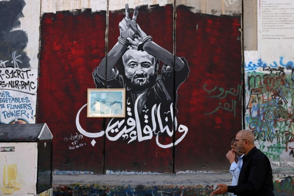 Men walk past a section of Israel’s separation barrier bearing an image of Palestinian Marwan Barghouti, who is being held in an Israeli jail, Bethlehem, occupied West Bank, Nov. 6, 2023. (AFP)