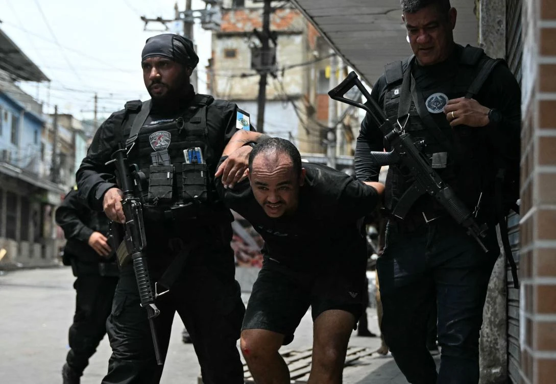 A suspect is escorted by police officers after being arrested during the Operacao Contencao (Operation Containment) at the Vila Cruzeiro favela, in the Penha complex, in Rio de Janeiro, on Oct. 28, 2025. (AFP)