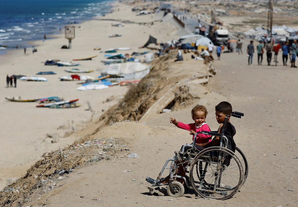 Displaced Palestinian children sit in a wheelchair by the side of a road in the central Gaza Strip. (Reuters)