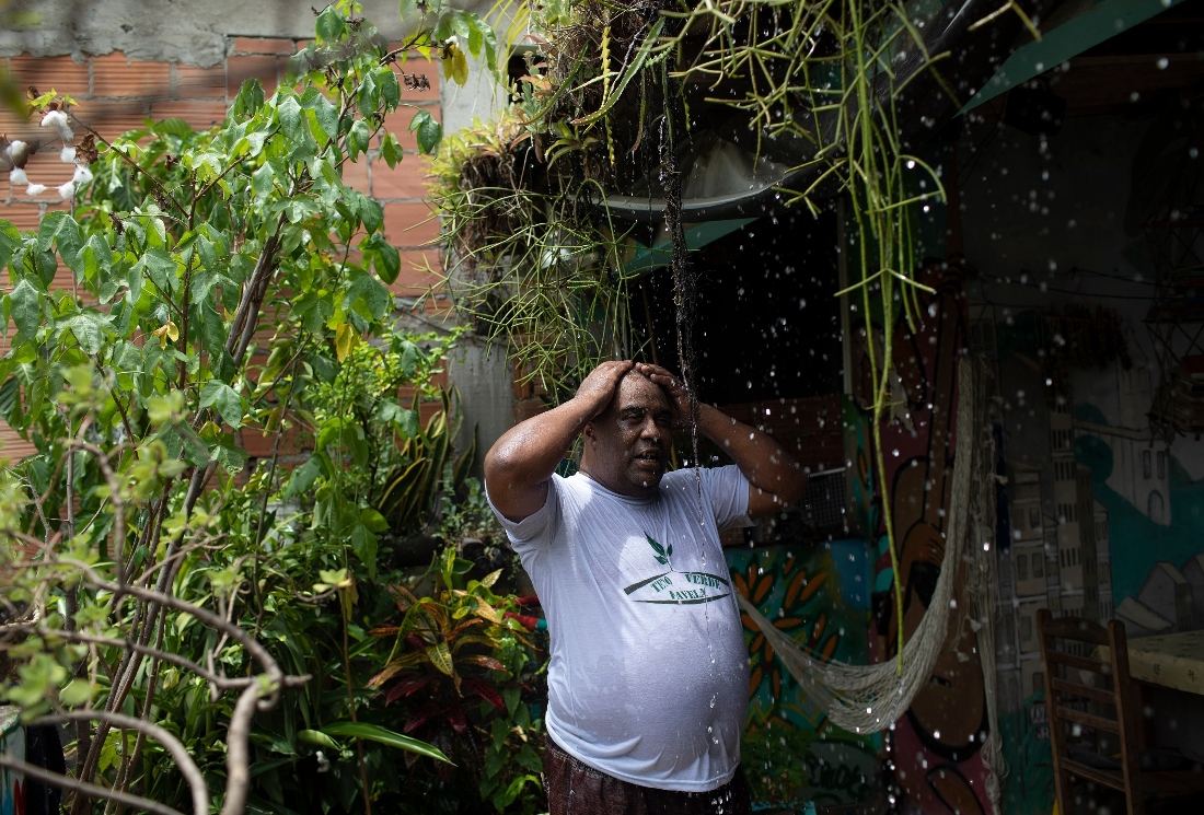 Luis Cassiano cools off with water that falls from his green roof at his home in Arara, a poor neighborhood, in Rio de Janeiro. (AP)
