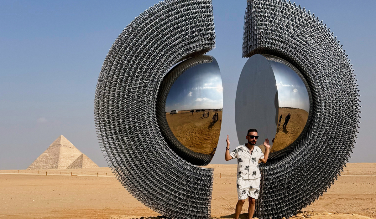 A visitor poses with the installation of Turkish artist Mert Age Kose, "The Shen", during the fifth edition of "Forever Is Now" contemporary art exhibition at the historical site of the Giza Pyramids, in Giza, Egypt, Tuesday, Nov. 11, 2025. (AP)