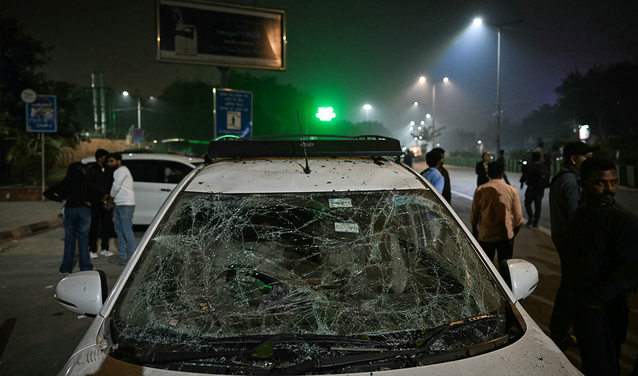 People gather beside a damaged vehicle at the blast site after an explosion near the Red Fort in the old quarters of Delhi on November 10, 2025. (AFP)