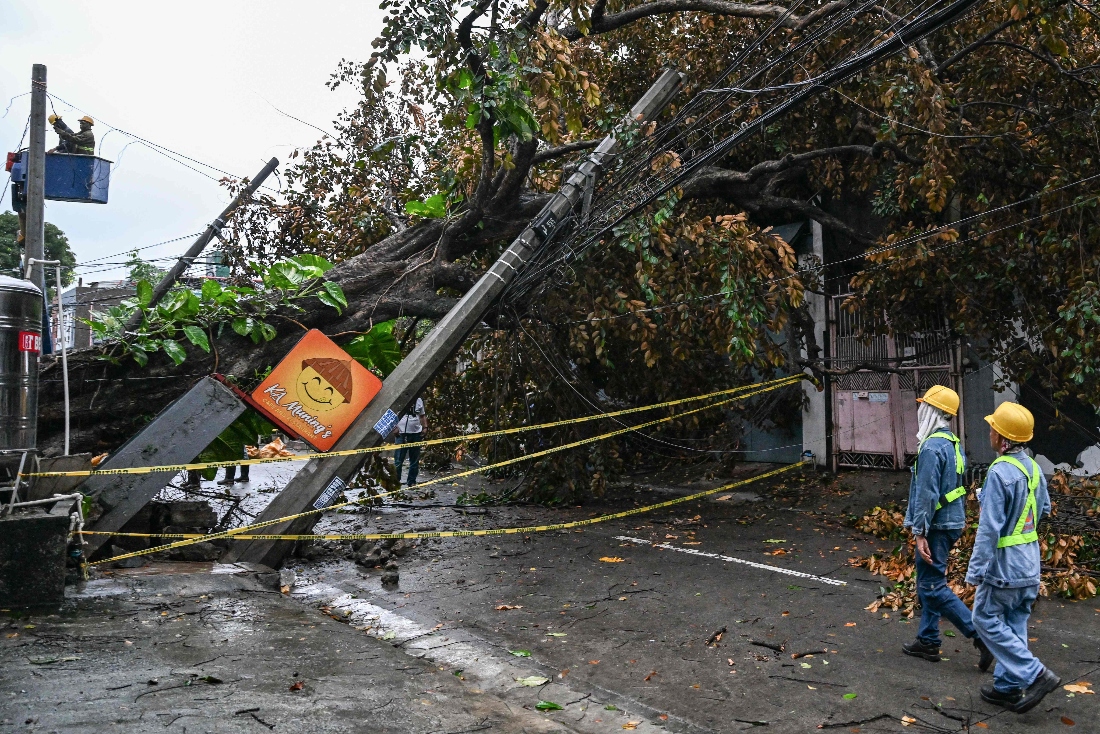 Workers inspect a fallen post and a tree along a street in Quezon City, Metro Manila. (AFP)