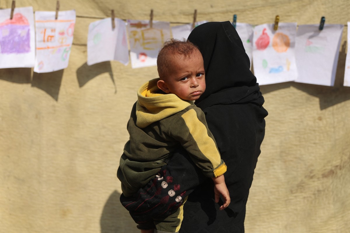 A woman carrying a child looks at an exhibition featuring a collection of drawings by children and women in Gaza. Amany faces giving up her UK scholarship because she cannot bring her family with her. (AFP/File Photo)