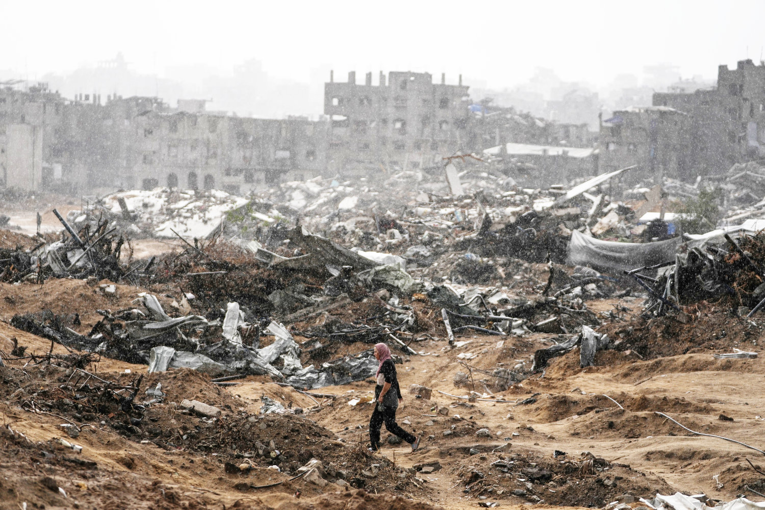 A Palestinian woman walks through a rainstorm past buildings destroyed in Israeli strikes in the Sheikh Radwan neighborhood of Gaza City. (AP)