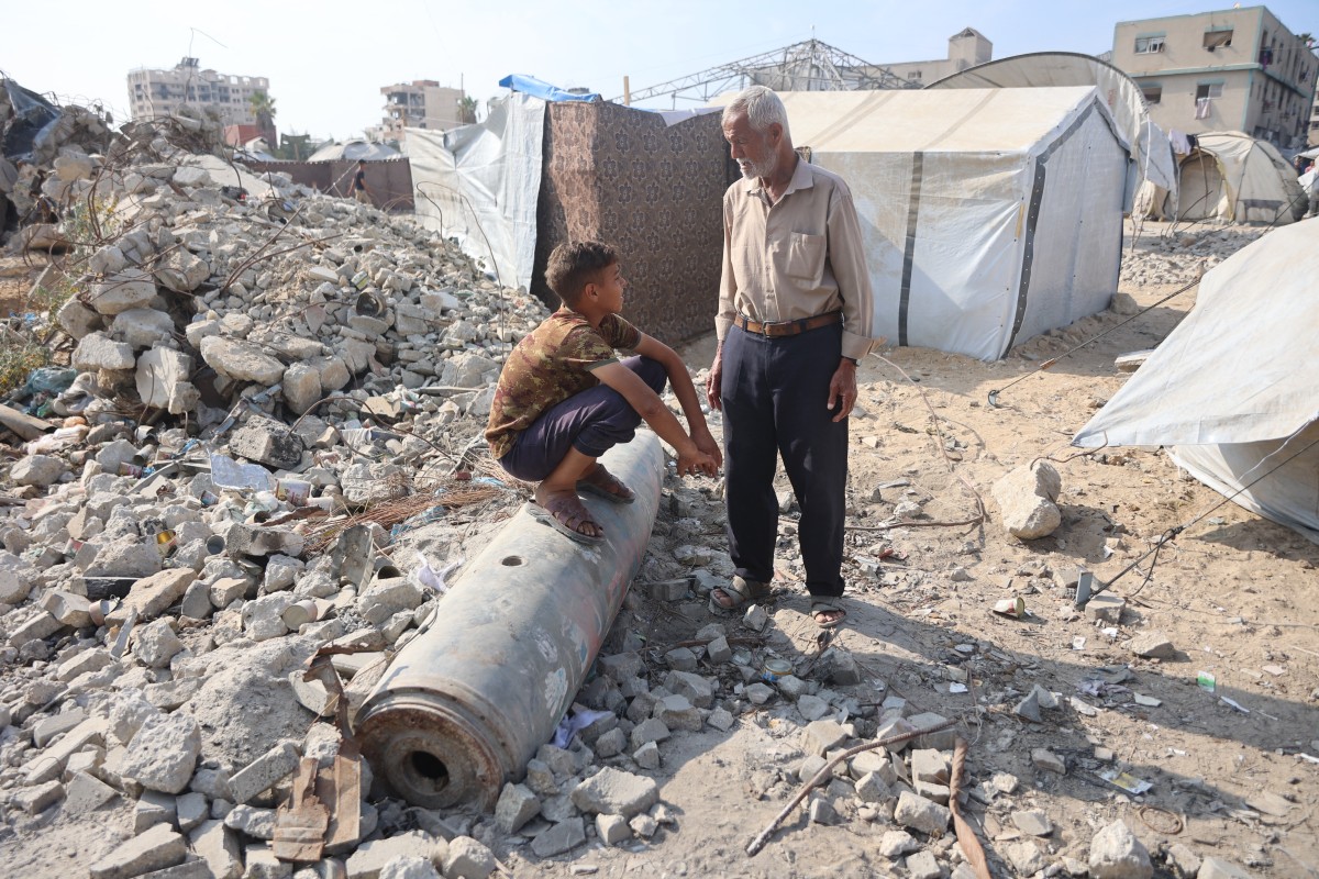 A Palestinian man speaks to a boy sitting on an unexploded missile in the Al-Rimal neighborhood of Gaza City, Nov. 12, 2025. (AFP)