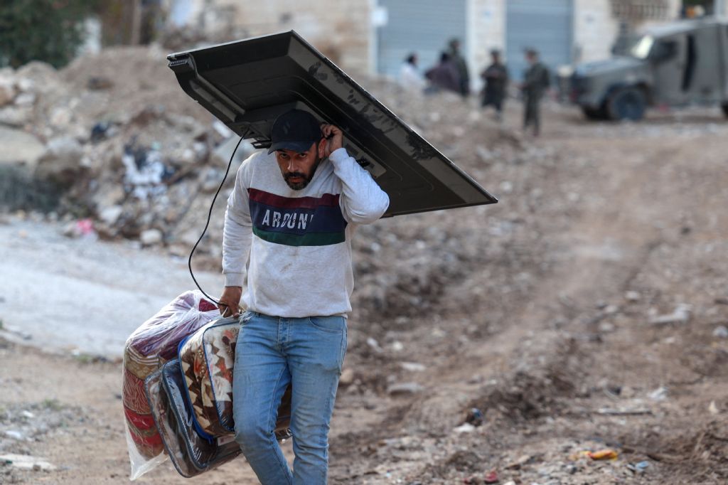 A Palestinian man carries his belongings as he evacuates his home during an Israeli army raid on the Jenin refugee camp in the occupied West Bank on November 27, 2025. (AFP)