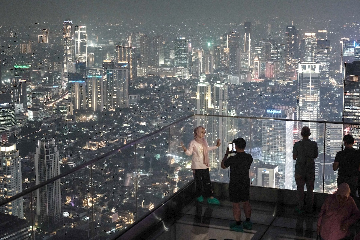 People stand on a transparent-floor deck of an observatory claimed to be Indonesia's highest, at the Thamrin Nine building in Jakarta on July 24, 2025. (AFP)