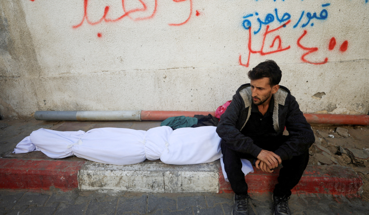 A mourner sits next to the body of a Palestinian who, according to medics, was killed in overnight Israeli strikes, at Al-Shifa Hospital in Gaza City, November 20, 2025. (REUTERS)
