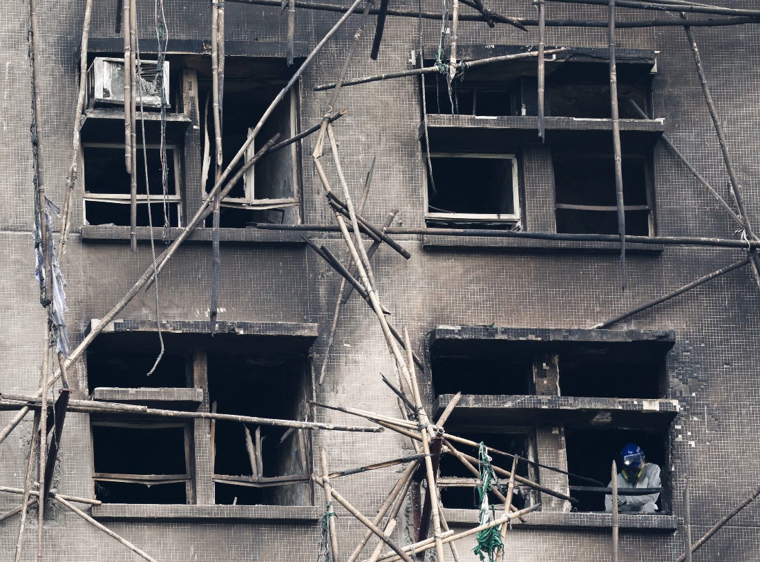 A police officer wearing personal protective equipment works near a window of a burned building at the Wang Fuk Court housing complex after the deadly fire, in Tai Po, Hong Kong, China. (Reuters)