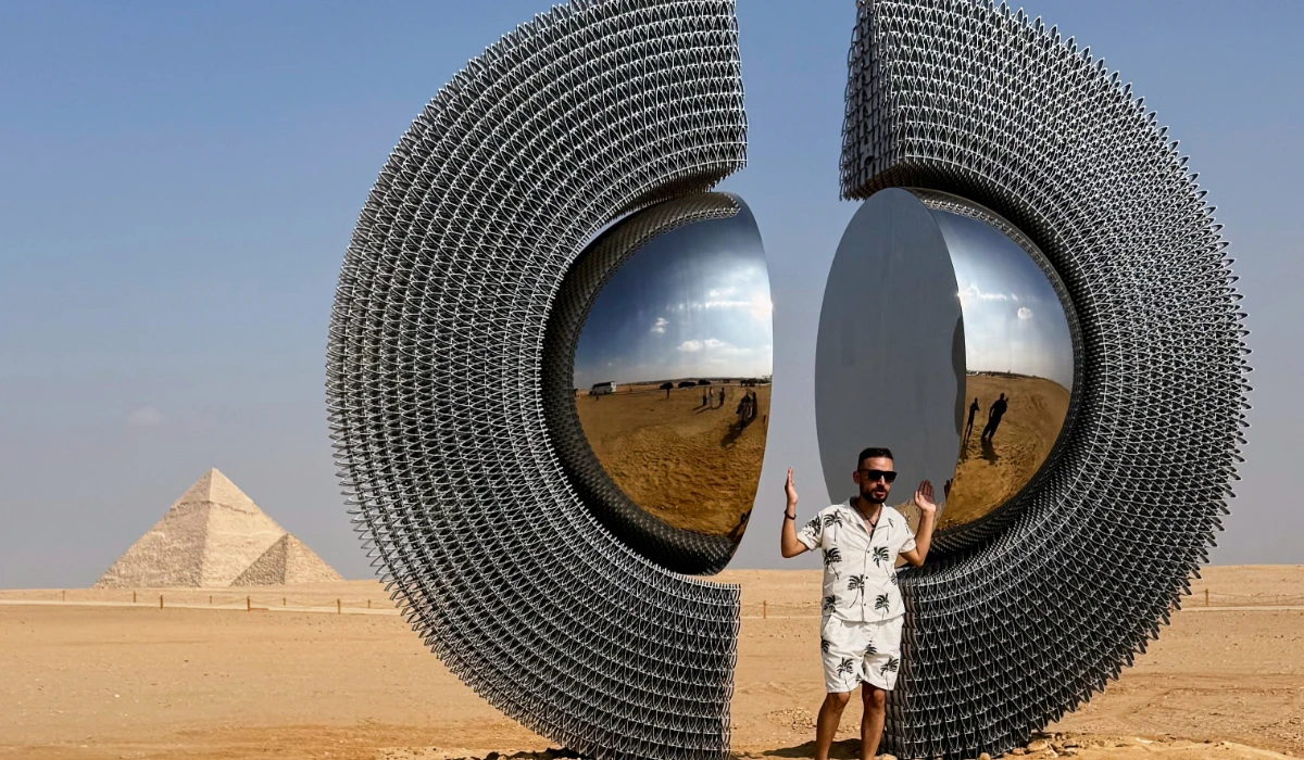 A visitor poses with the installation of Turkish artist Mert Age Kose, "The Shen", during the fifth edition of "Forever Is Now" contemporary art exhibition at the historical site of the Giza Pyramids, in Giza, Egypt, Tuesday, Nov. 11, 2025. (AP)