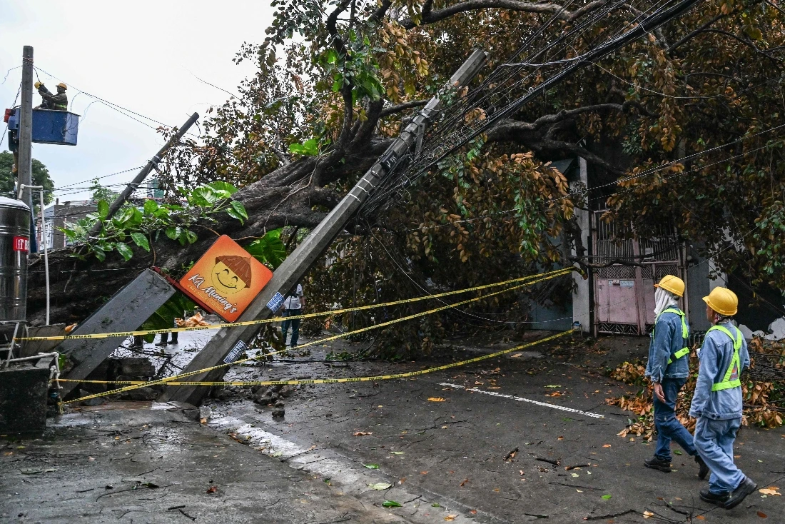 Workers inspect a fallen post and a tree along a street in Quezon City, Metro Manila. (AFP)