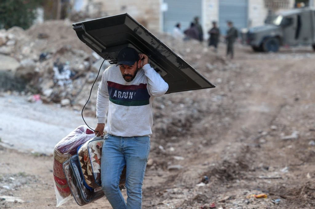 A Palestinian man carries his belongings as he evacuates his home during an Israeli army raid on the Jenin refugee camp in the occupied West Bank on November 27, 2025. (AFP)