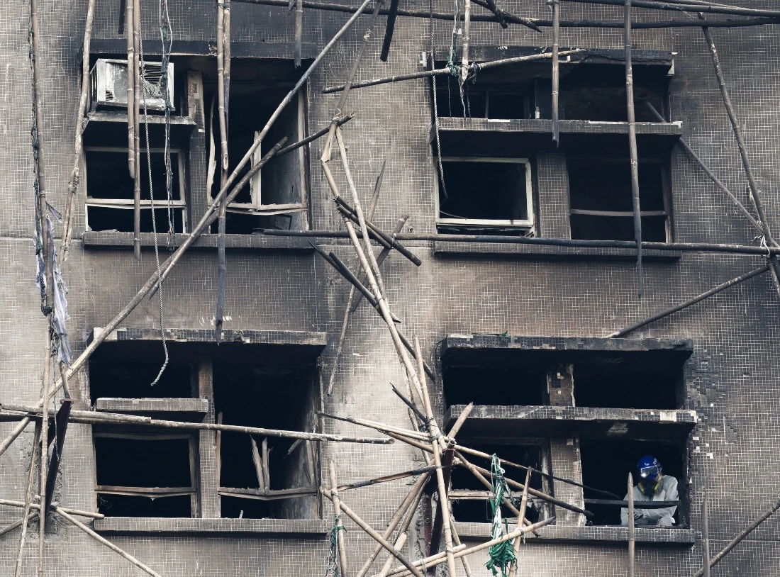 A police officer wearing personal protective equipment works near a window of a burned building at the Wang Fuk Court housing complex after the deadly fire, in Tai Po, Hong Kong, China. (Reuters)