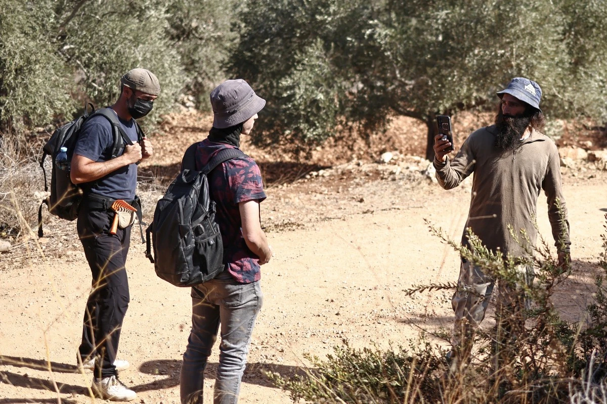 An Israeli settler (R) uses his mobile phone as he records foreign volunteers (L) in an olive grove, after disrupting Palestinian farmers’ olive harvest near the Israeli occupied Palestinian West Bank village of Turmus Ayya, Oct. 28, 2025. (AFP)
