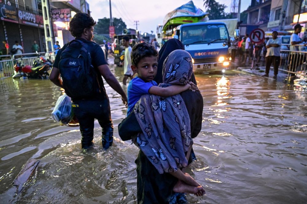 A woman carrying a child wades through a flooded street after heavy rainfall in Wellampitiya on the outskirts of Colombo, Sri Lanka, on Nov. 30, 2025. (AFP)