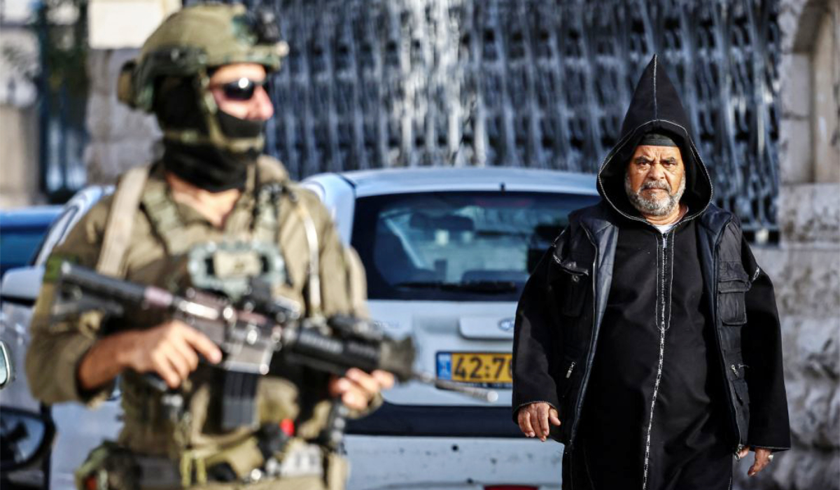 A Palestinian Muslim man, dressed in traditional Islamic clothes walks behind an Israeli soldier during a raid on the Ali Mosque in Ramallah, in the occupied West Bank, on December 9, 2025. (AFP)