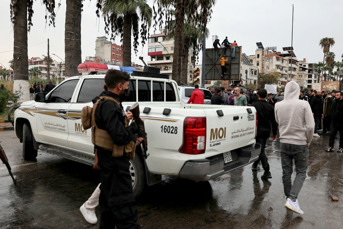 Syrian Internal Security officers stand near their vehicle, as people take part in a protest in al-Azhari Square, Latakia, Syria. (AFP)