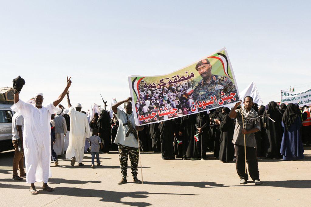 Sudanese men hold up a banner that showing an image of Sudanese regular army chief Abdel Fattah al-Burhan. (Photo by MOGTABA KANARY / AFP)