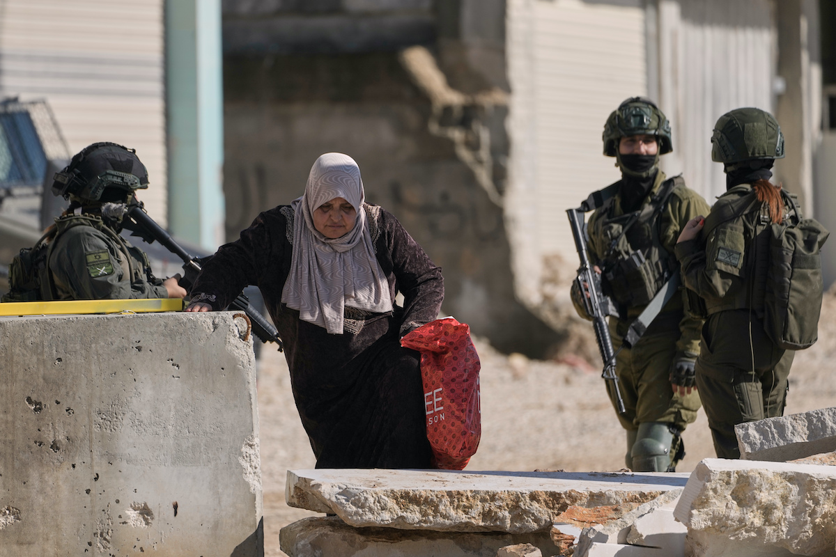 A Palestinian woman walks past Israeli soldiers as she carries her belongings ahead of a planned home demolitions in the refugee camp of Nur Shams, in the West Bank city of Tulkarem on Wednesday. (AP)
