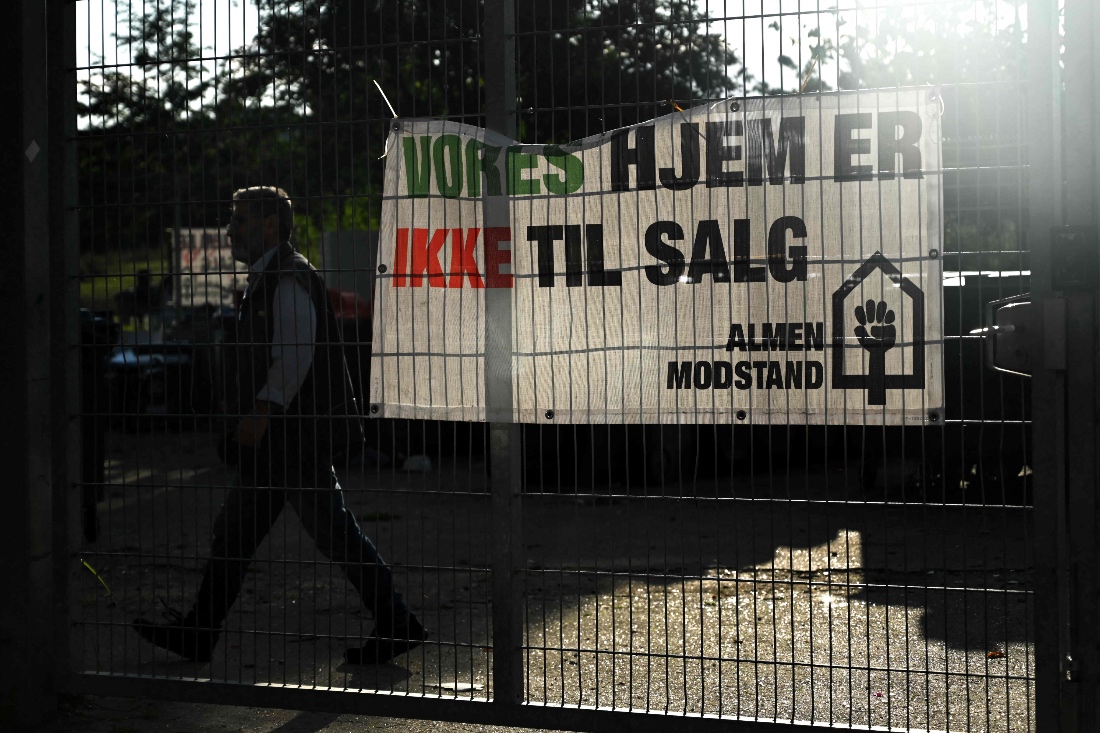 A man walks past a banner with a text reading 'Our homes are not for sale' in the courtyard of Mjolnerparken housing estate in Copenhagen, Denmark. (AFP)