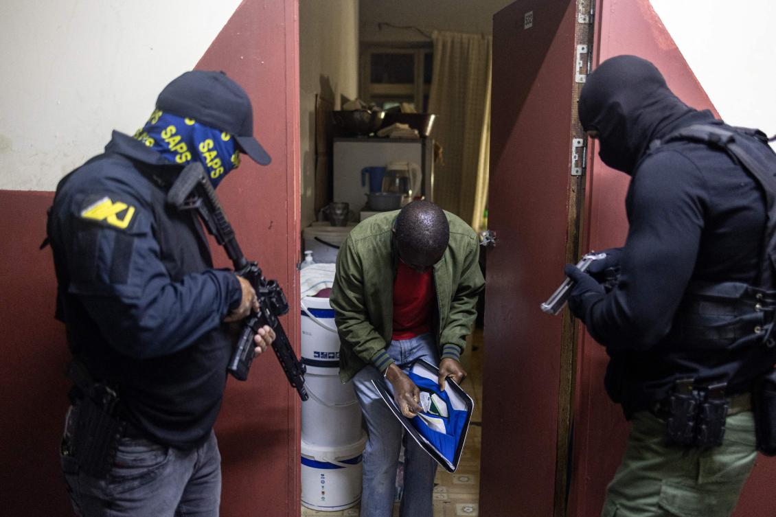 South African Police Department (SAPS) Anti-kidnapping unit officers stand guard as a resident looks through a folder before presenting his documents during a raid in a highjacked building in the Johannesburg CBD on December 18, 2025. (Photo by EMMANUEL CROSET / AFP)