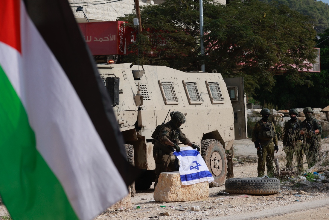 An Israeli soldier places the Israeli flag on a bollard at the entrance of the Nur Shams Palestinian refugee camp, in the Israeli-occupied northern West Bank. (AFP)