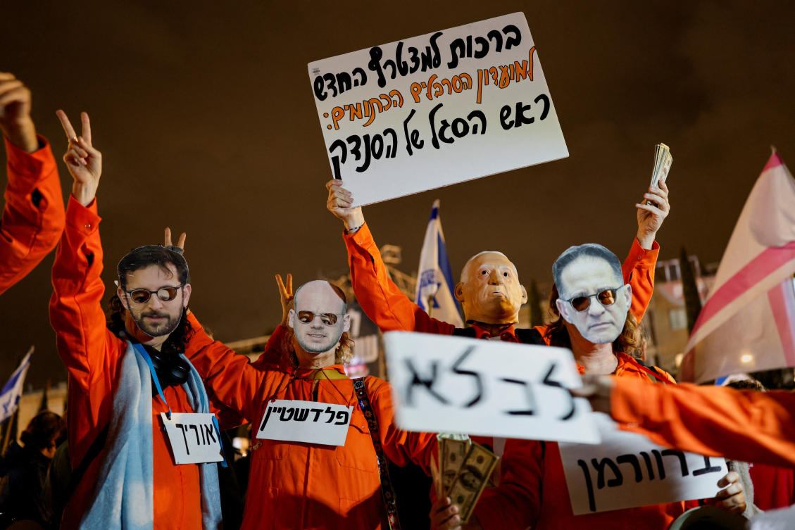 Protesters wearing orange jumpsuits and holding mock dollar bills take part in a demonstration against Israeli Prime Minister Benjamin Netanyahu and his government, in Tel Aviv, Israel, December 27, 2025. The sign at the top reads: "Congratulations to the winners of the fire sale: the corrupt movie producers". Another sign reads: "Palestine". REUTERS/Amir Cohen