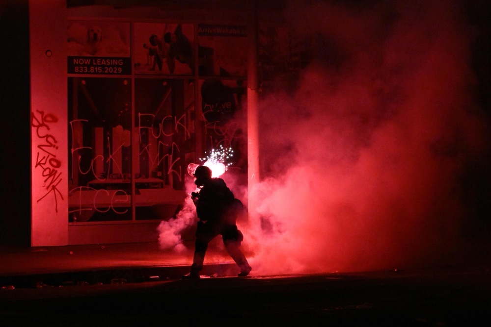 A firework explodes behind a police officer in riot gear during a protest in response to federal immigration operations in the Little Tokyo neighborhood of downtown Los Angeles. (AFP/File)