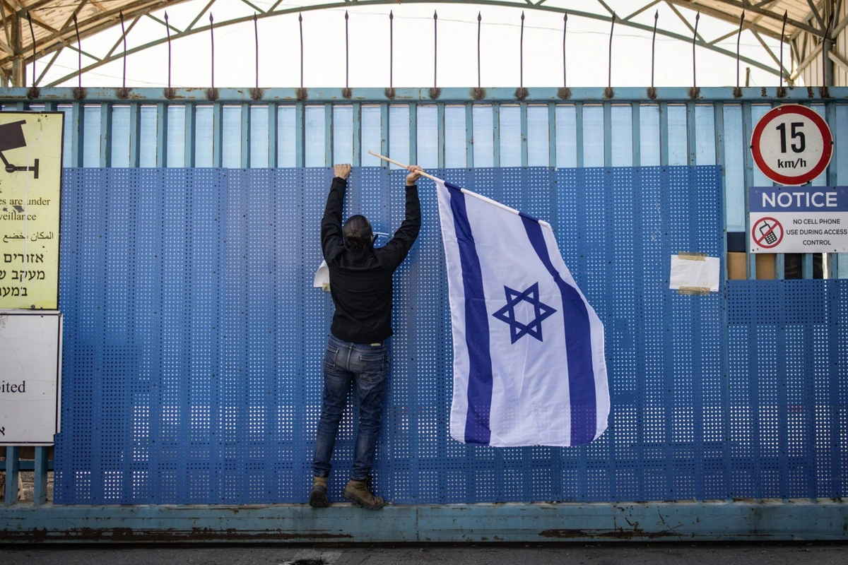 An Israeli right wing activist hangs a national flag at the shuttered gate of the UNRWA's West Bank Field Office in East Jerusalem, Jan. 30, 2025. (AFP)