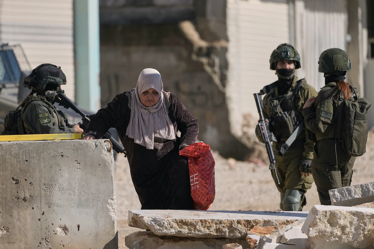A Palestinian woman walks past Israeli soldiers as she carries her belongings ahead of a planned home demolitions in the refugee camp of Nur Shams, in the West Bank city of Tulkarem on Wednesday. (AP)