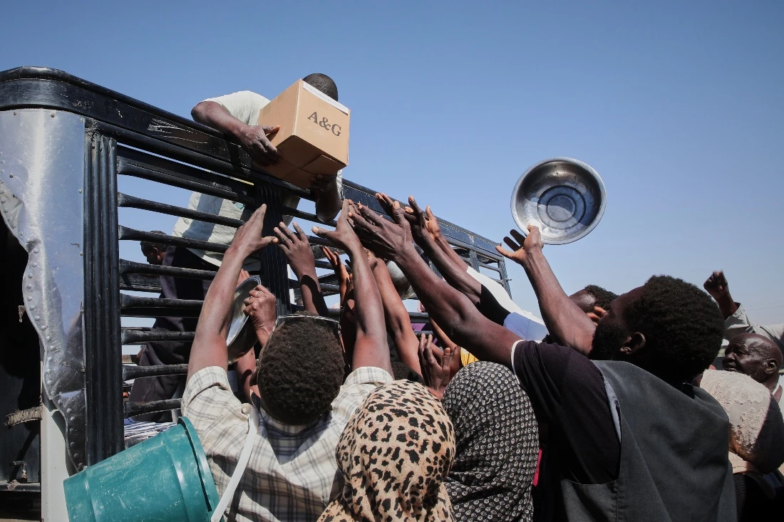 Sudanese families displaced from El-Fasher reach out as aid workers distribute food supplies at the newly established El-Afadh camp in Al Dabbah, in Sudan's Northern State. (AP)