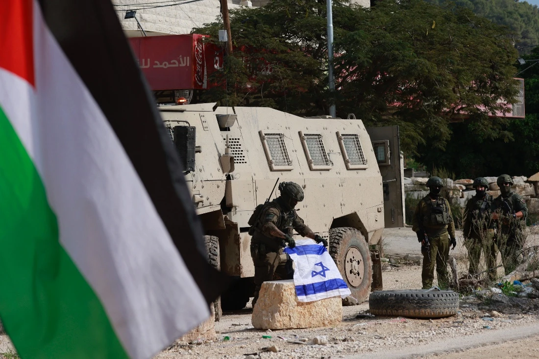 An Israeli soldier places the Israeli flag on a bollard at the entrance of the Nur Shams Palestinian refugee camp, in the Israeli-occupied northern West Bank. (AFP)