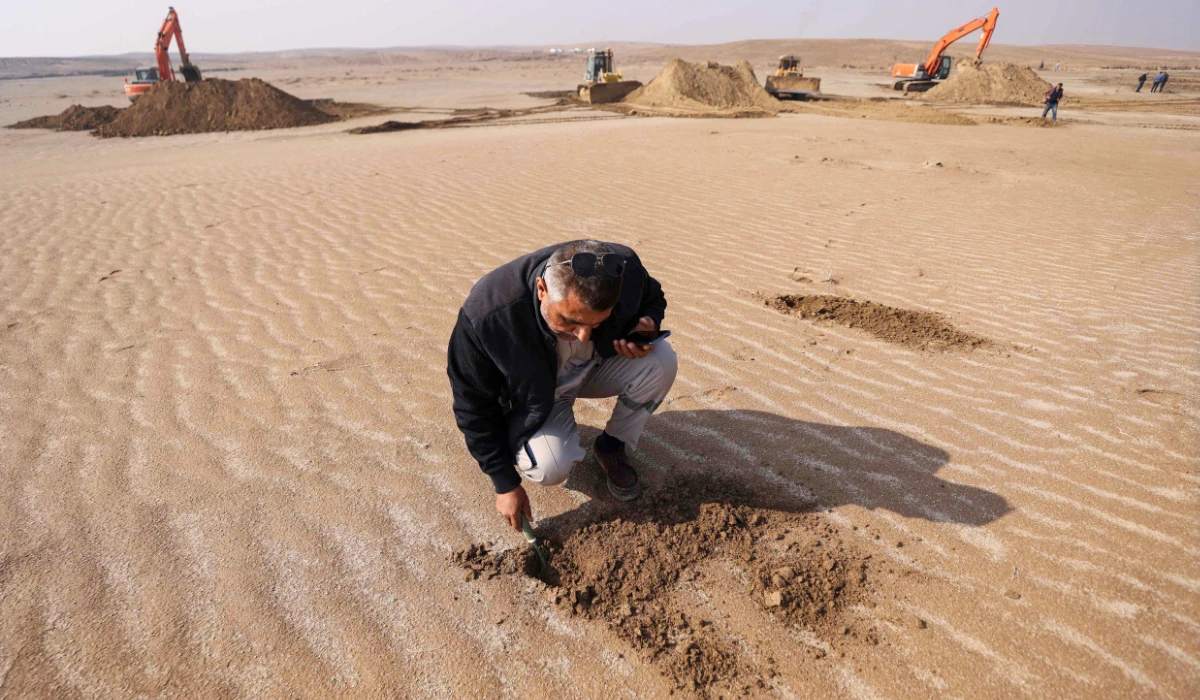 An Iraqi engineer examines the soil as excavators clear sand dunes and extract clay in the desert south of Samawah on December 21, 2025. (AFP)