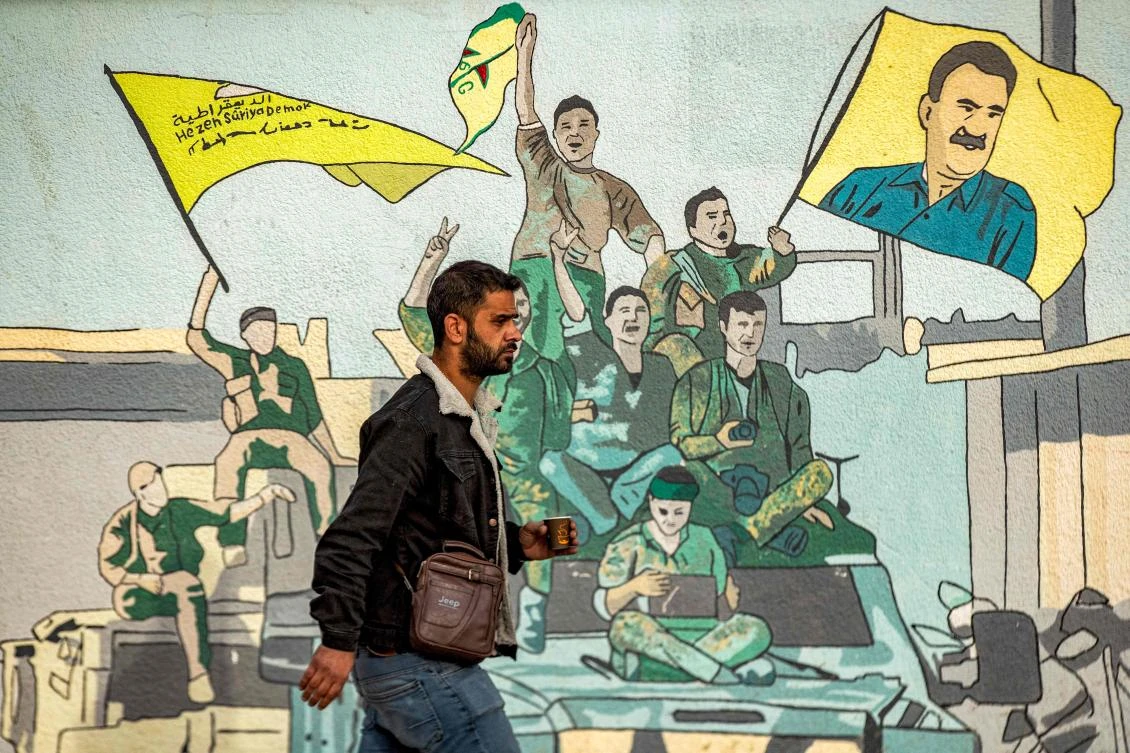 A man walks past a mural depicting supporters of the Syrian Democratic Forces (SDF), one of them raising a flag showing the face of Abdullah Ocalan. (Photo by Delil SOULEIMAN / AFP)