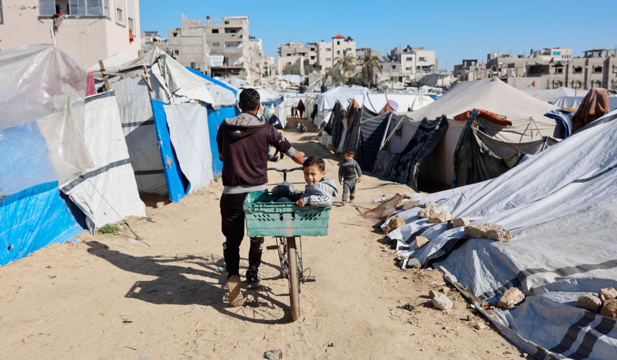 A child sits in a basket attached to a bicycle as a man pushes it past tent shelters in Gaza. (AFP)