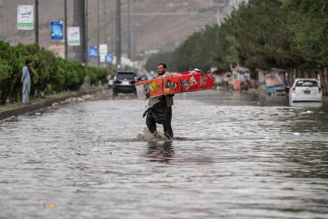 An Afghan shopkeeper carrying his belongings walks across a flooded road after heavy rainfall in Kabul on July 13, 2025. (File/AFP)