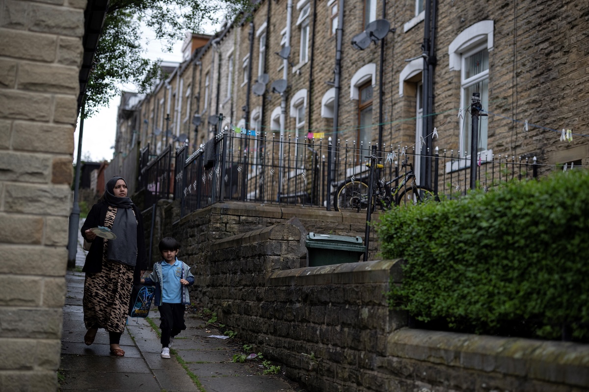 A woman and child walk along an alley past a terrace of houses in a residential area close to the town centre of Keighley, northwest England, on June 14, 2024. (FILE/AFP)