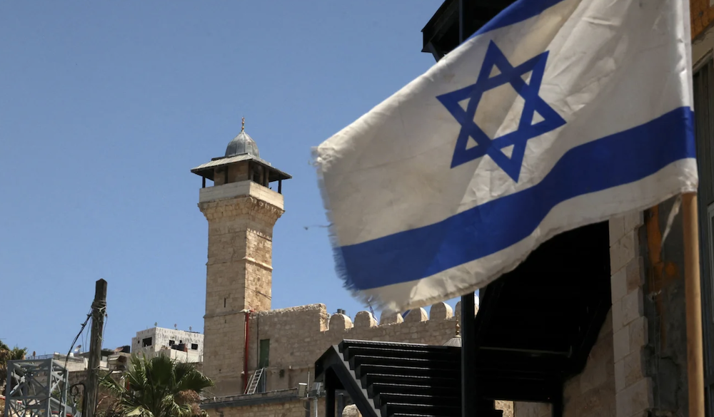 An Israeli flag flies in a street in front of the Ibrahimi Mosque in the occupied West Bank city of Hebron, on 26 May 2022. (AFP/File Photo)