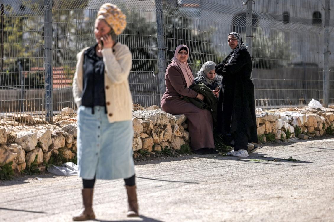 An Israeli settler (L) speaks on a phone as she stands near Palestinian women from the Ayoub Abdel-Basit al-Tamimi family, whose home was allegedly taken over by Israeli settlers overnight, in Hebron city near the Israeli settlement area of Tel Rumeida in the occupied West Bank on March 24, 2025. (FILE/AFP)