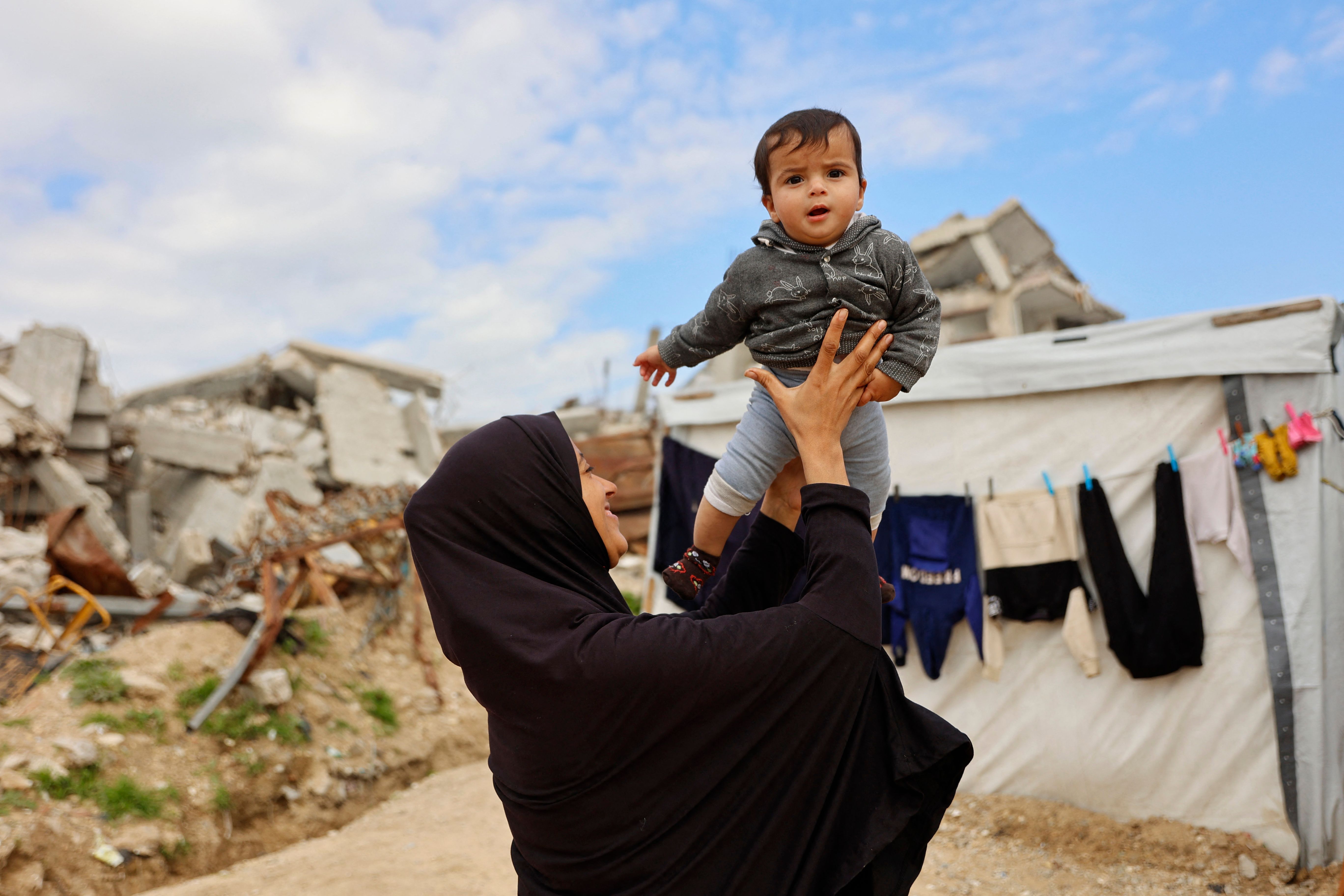 A displaced Palestinian mother plays with her child outside her tent shelter erected close to the rubble and debris of homes and businesses destroyed by the Israeli military in over two years of military strikes on the Gaza Strip enclave, in the Jabalia refugee camp, in the northern Gaza Strip on January 17, 2026. (AFP)