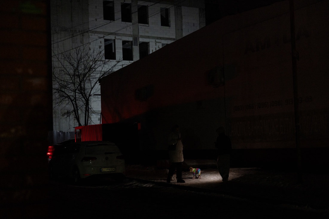 Residents including one with a headlamp walk a dog past residential buildings without electricity in Vyshgorod, Ukraine. (AFP)
